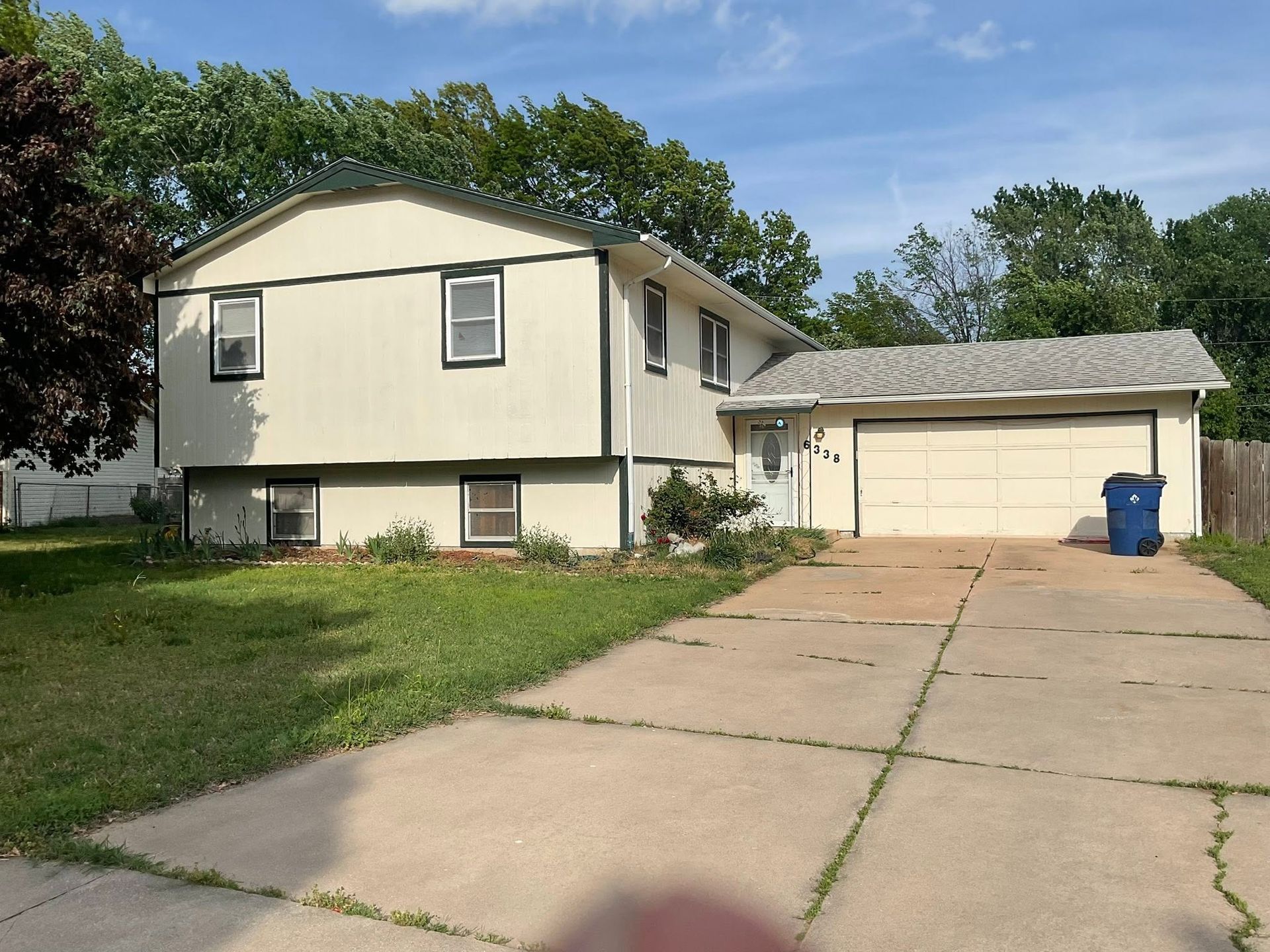 Single-story house with beige siding, attached garage, and long concrete driveway under a blue sky
