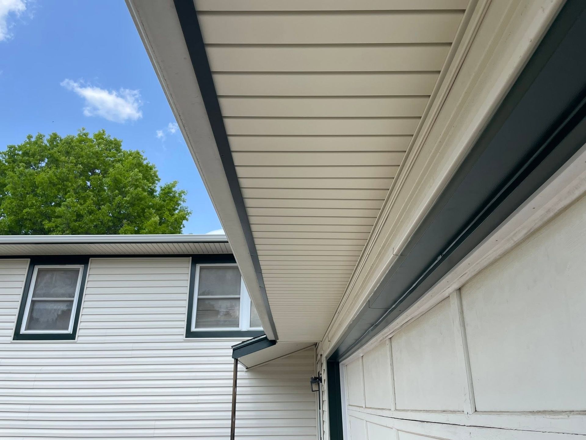 Close-up of house eaves and gutter beside a white siding wall under a blue sky