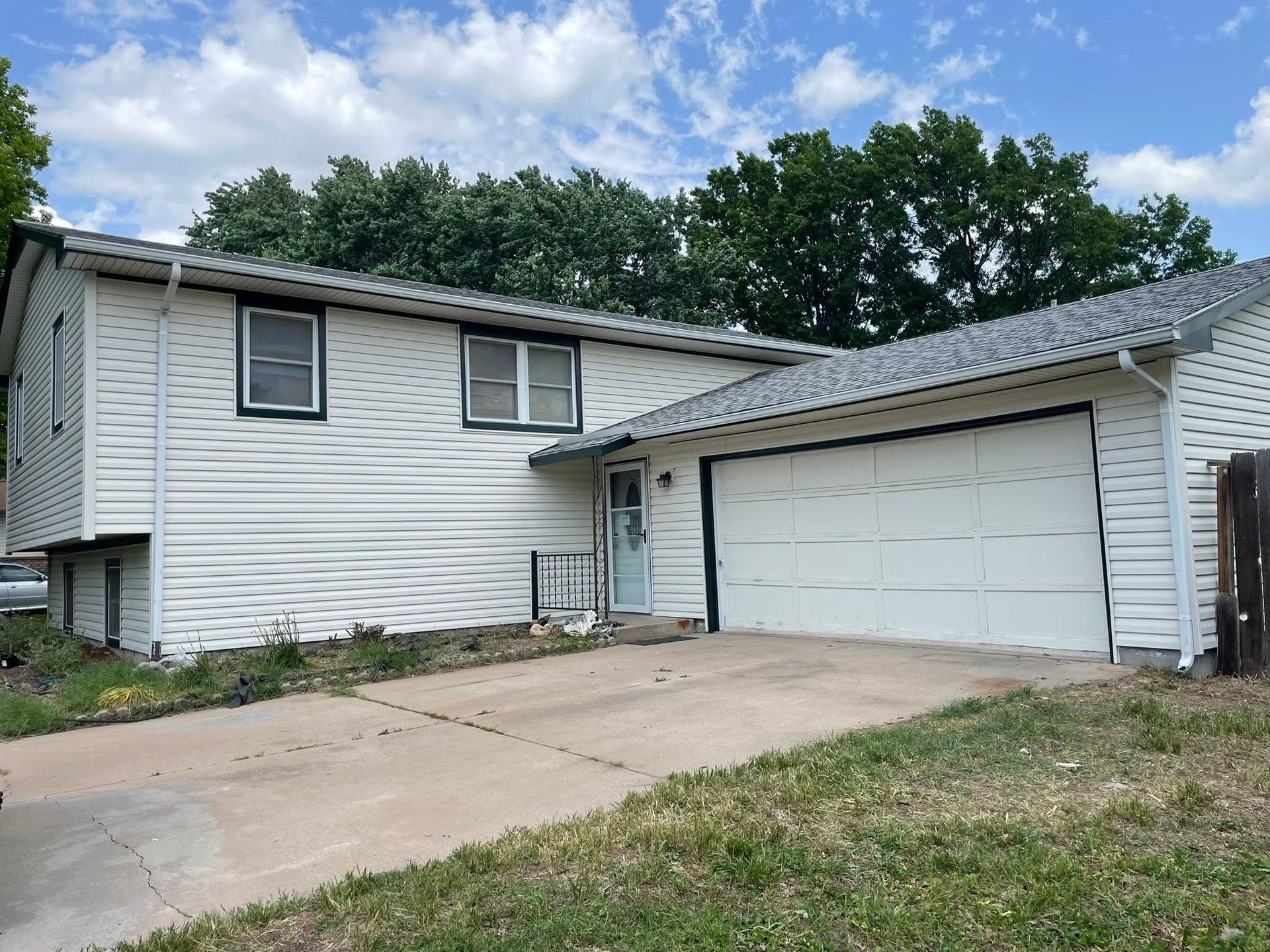 Suburban split-level house with white siding, attached garage, and concrete driveway under cloudy sky