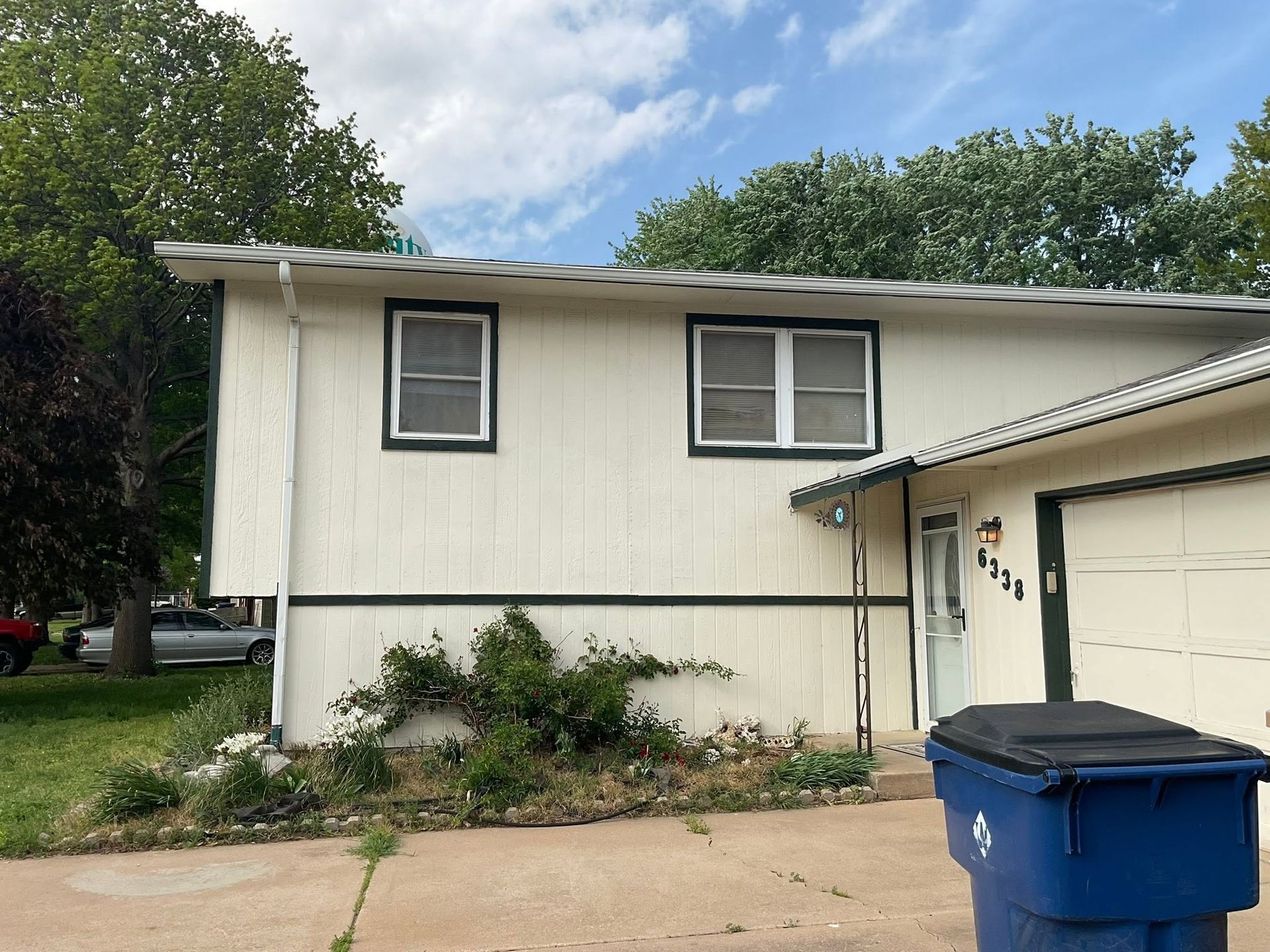 Suburban house exterior with beige siding, white garage, and a blue trash bin in the driveway