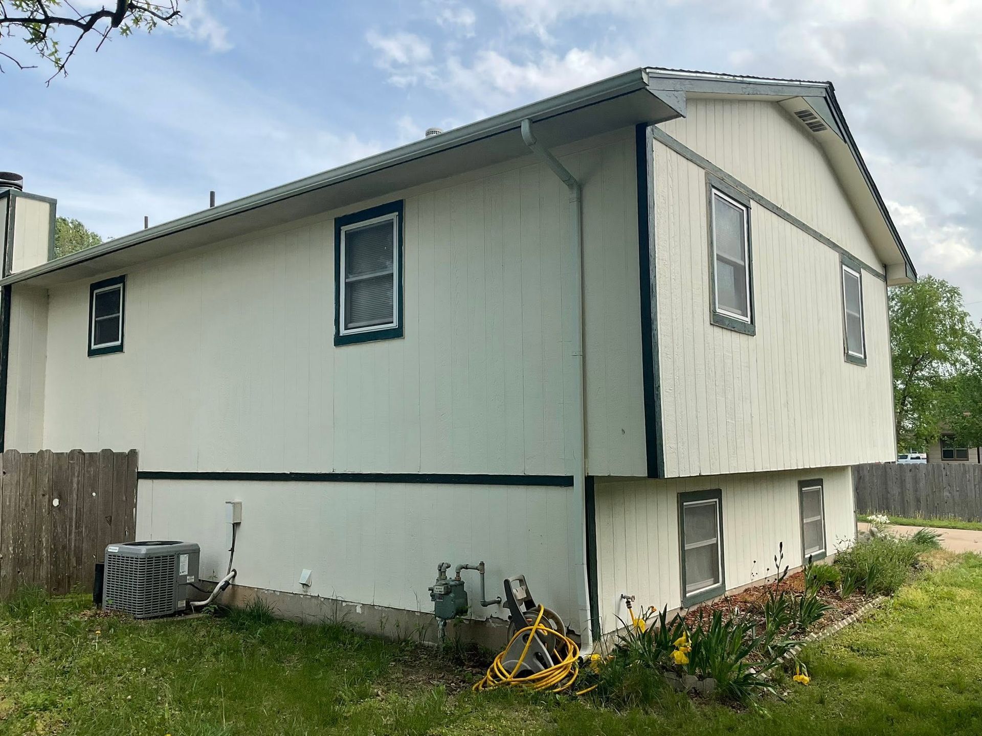 White two-story house with gray trim, small windows, and air conditioner units beside a wooden fence.