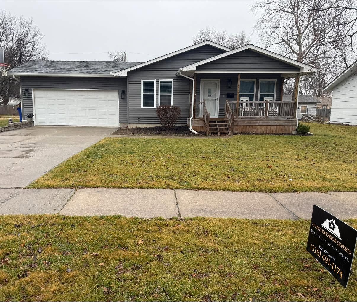 Single-story gray house with front porch, attached garage, and a yellow lawn on a cloudy day