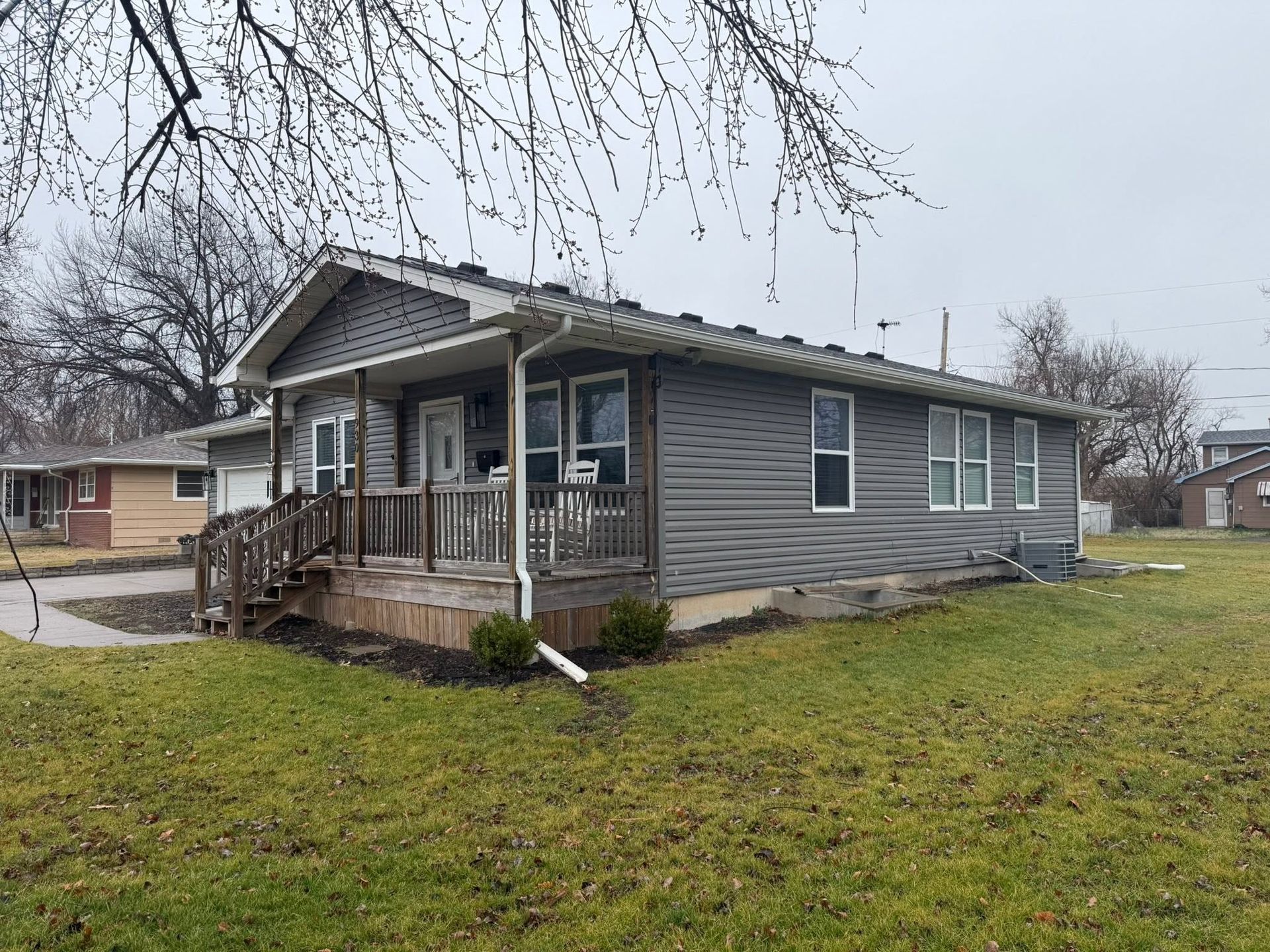 Gray single-story house with a front porch, in a grassy yard on an overcast day