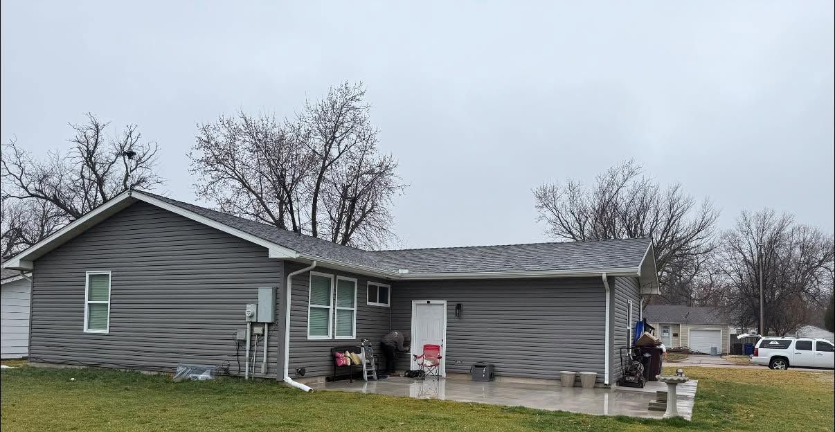 Gray single-story house with a porch and leafless trees in a cloudy yard