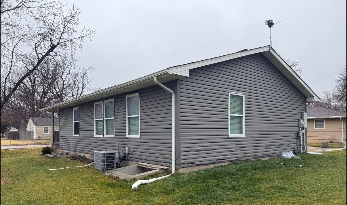 Gray vinyl-sided single-story house with white trim and a small front lawn under an overcast sky