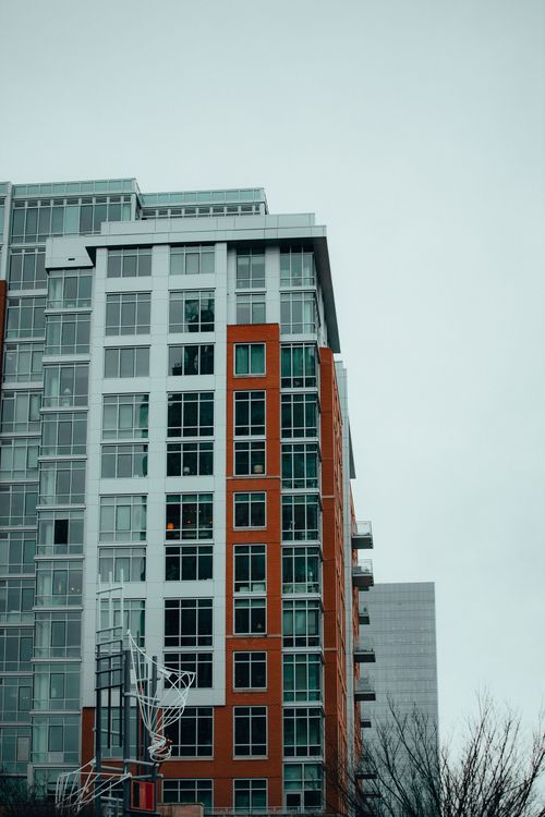 Tall modern apartment building with orange and gray facade against an overcast sky