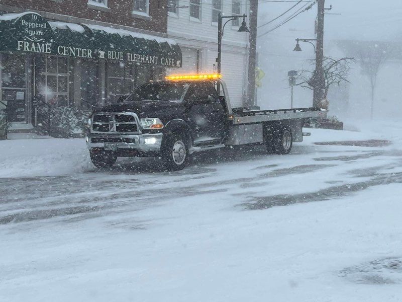 A tow truck is driving down a snowy street.