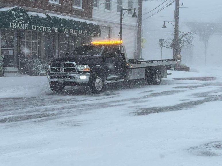 A tow truck is driving down a snowy street.