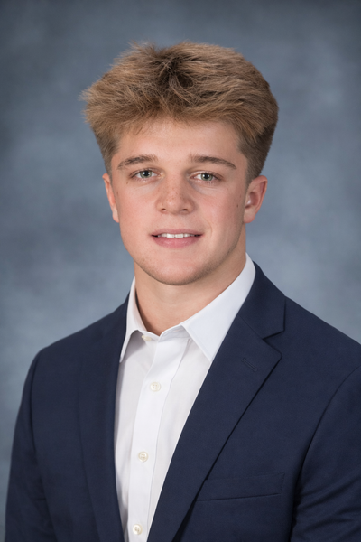 Studio portrait of a young man in a navy blazer and white shirt against a gray background