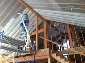 Worker on a ladder installing insulation in a house under construction