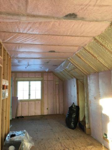 Insulated attic room with pink foam walls, sloped ceiling, and a small window at the far end.