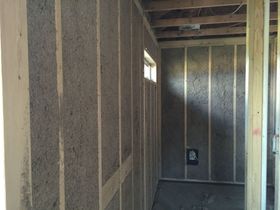 Unfinished interior of a small framed room with exposed insulation, wall studs, and a small window.