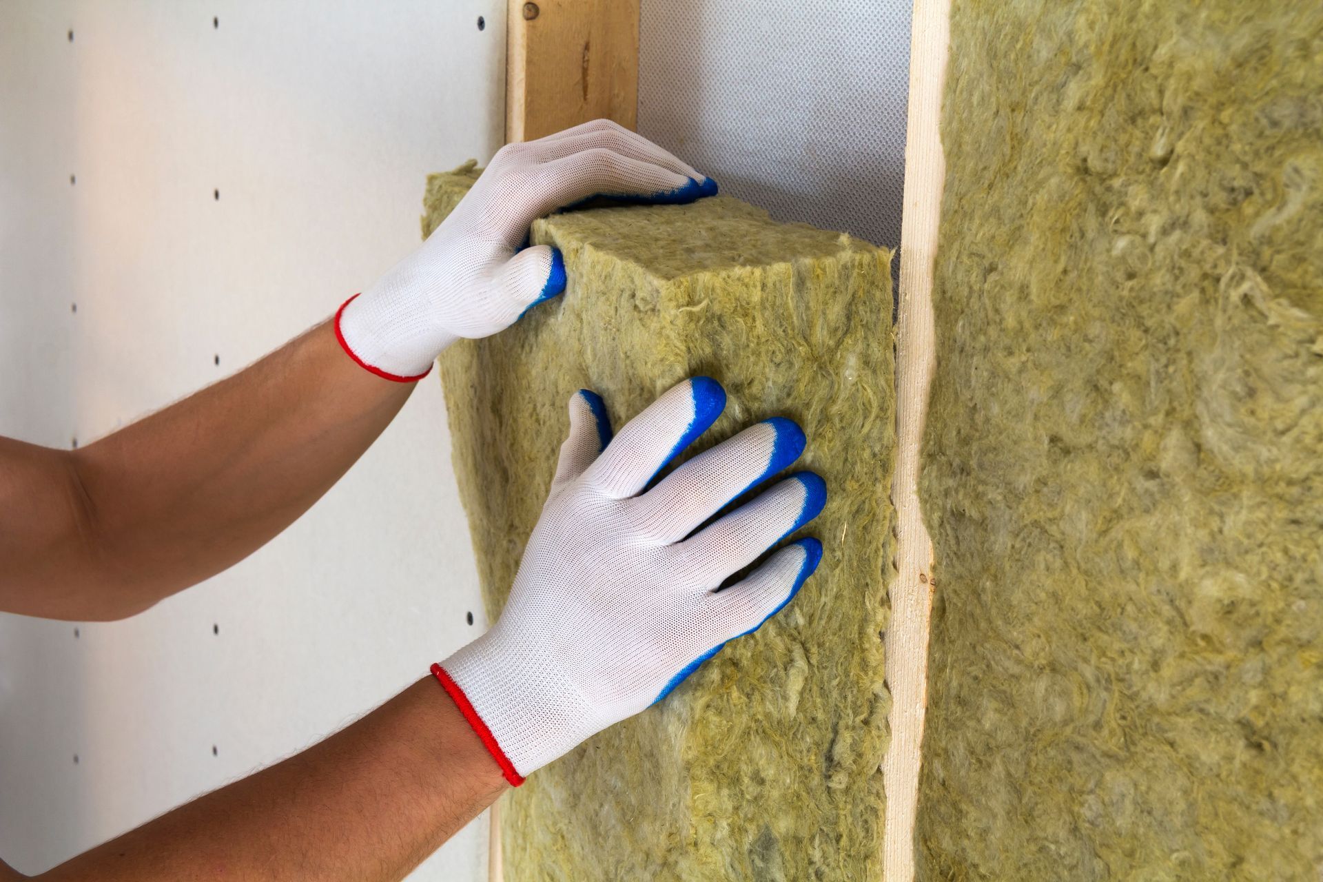 Hands in gloves installing insulation in a wall cavity.