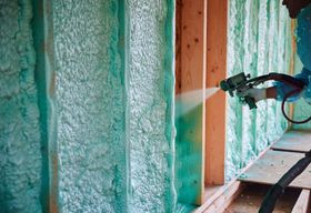 Person spraying green spray foam insulation into a wall cavity.