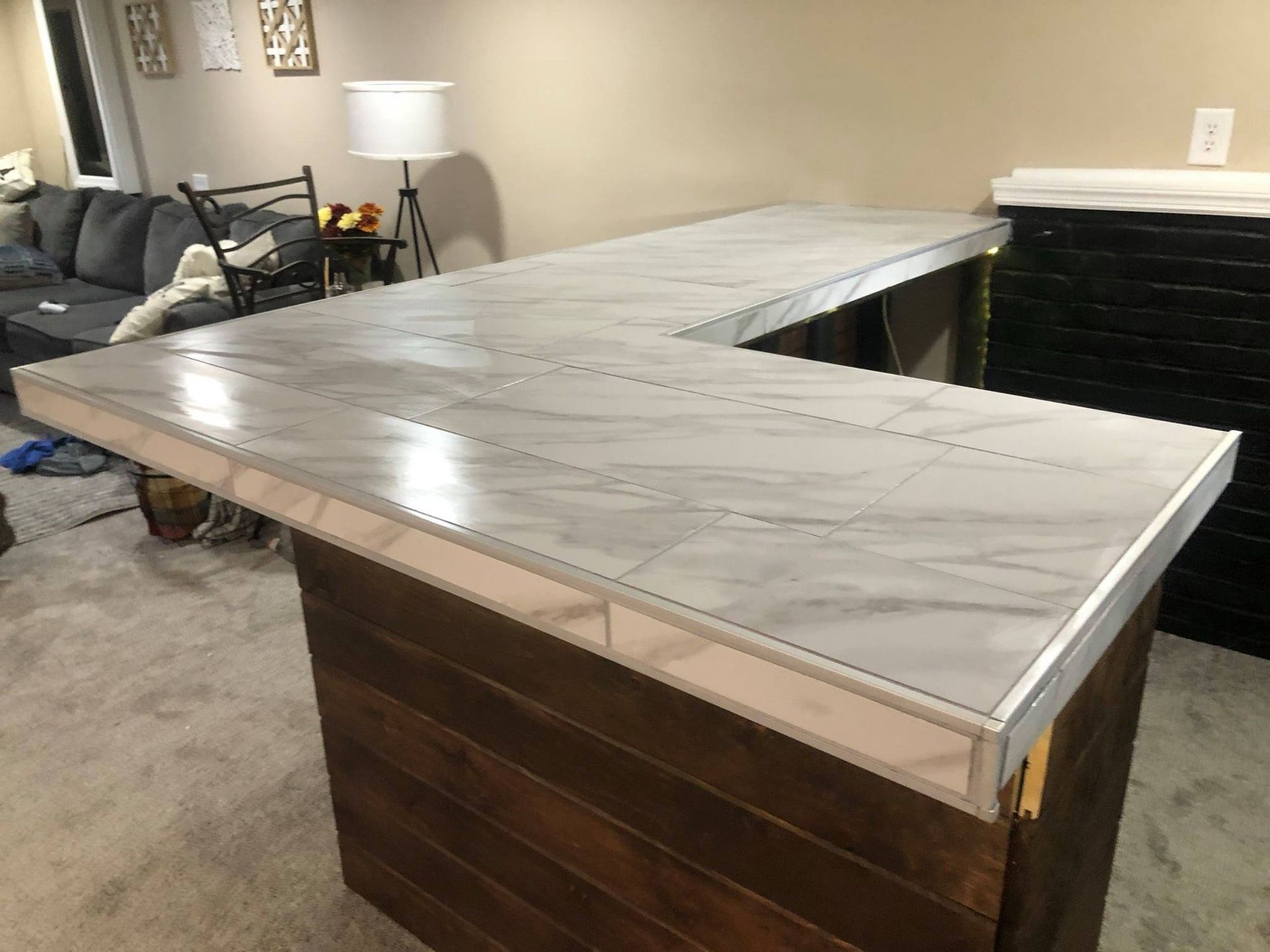 An L-shaped wooden bar with a marble-patterned countertop in a living room setting.