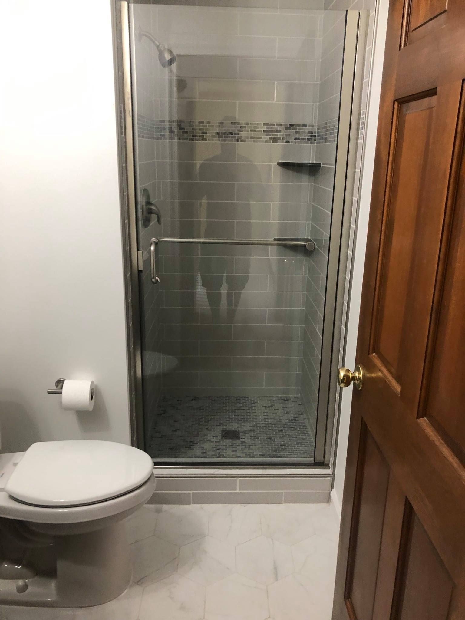 A bathroom with a toilet and a tiled glass-door shower stall next to a wooden door.