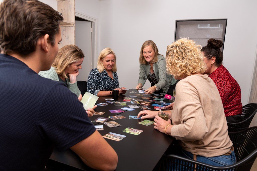 Een groep mensen zit rond een zwarte tafel een kaartspel te spelen in een lichte, moderne ruimte.