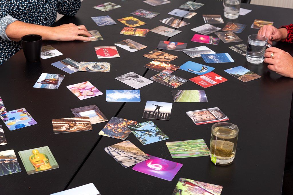 Mensen spelen een kaartspel aan een grote zwarte tafel vol kleurrijke kaarten met afbeeldingen.