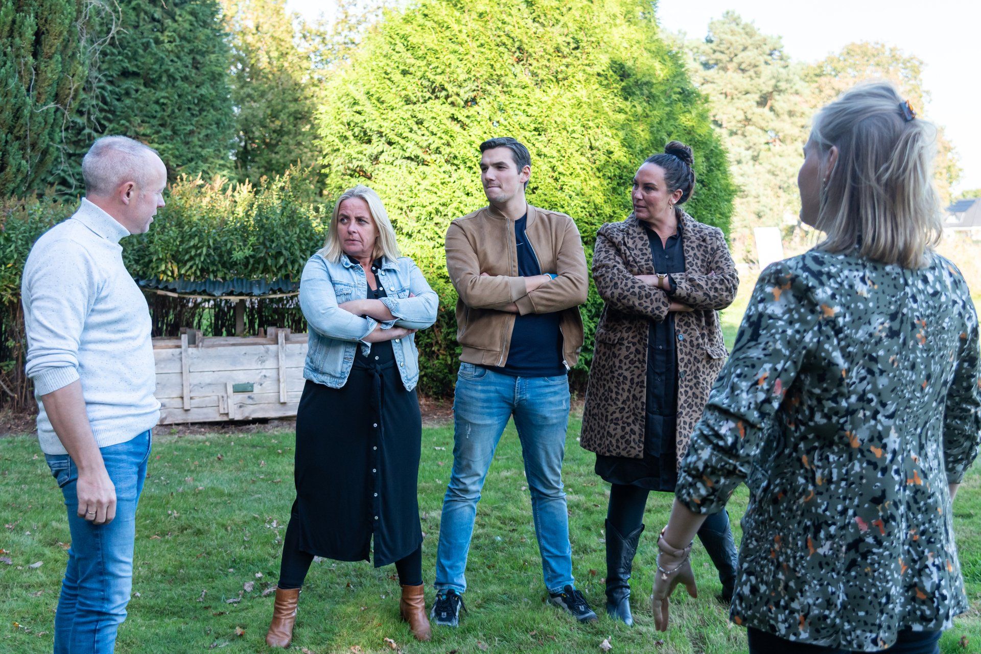 Een groep van vijf mensen staat buiten op een grasveld en voert een informeel gesprek.