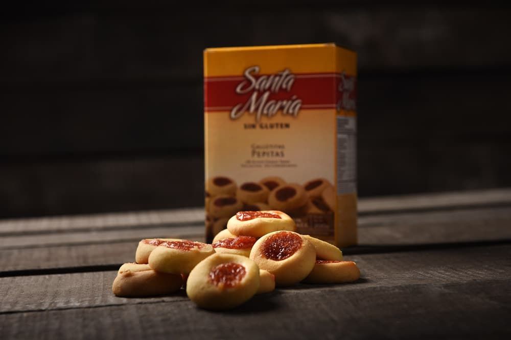 Una caja amarilla de galletas sin gluten de Santa María colocada detrás de una pequeña pila