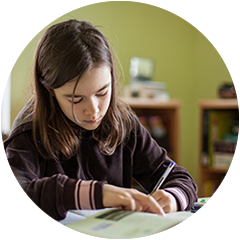 a young girl is sitting at a desk writing in a notebook .