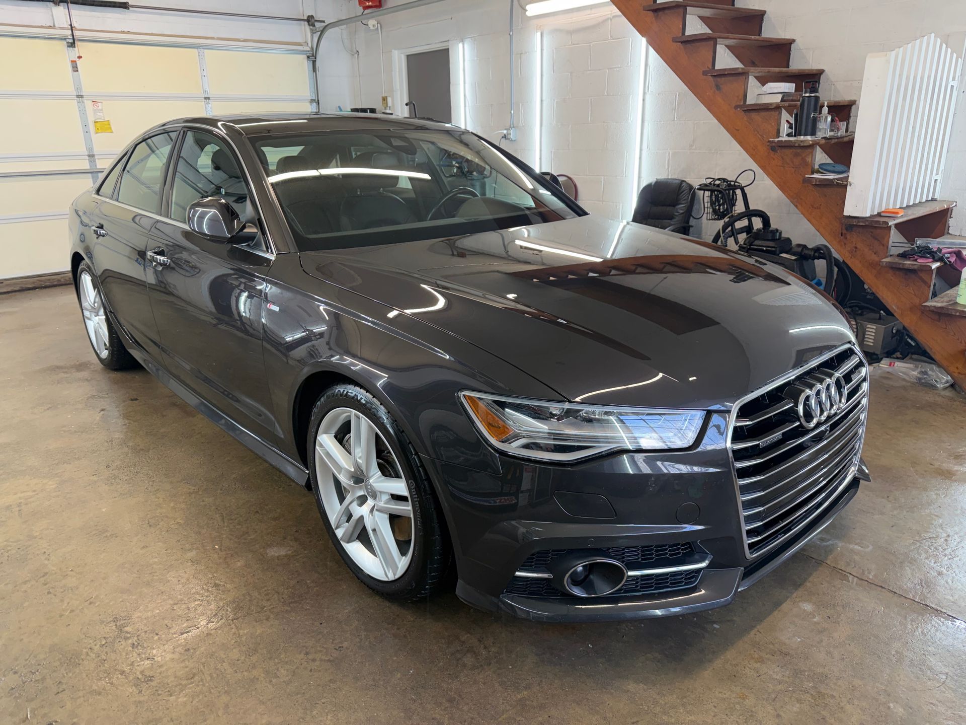 Black Audi sedan parked inside a garage beside a wooden staircase