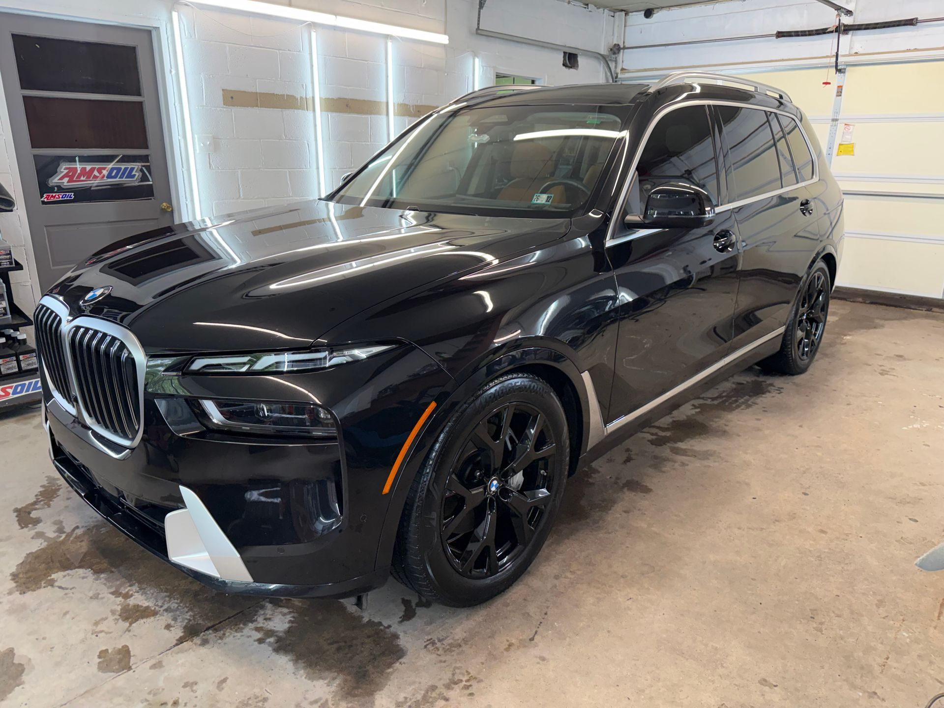 Black BMW SUV in a garage, front-left view, with black wheels and chrome grille.