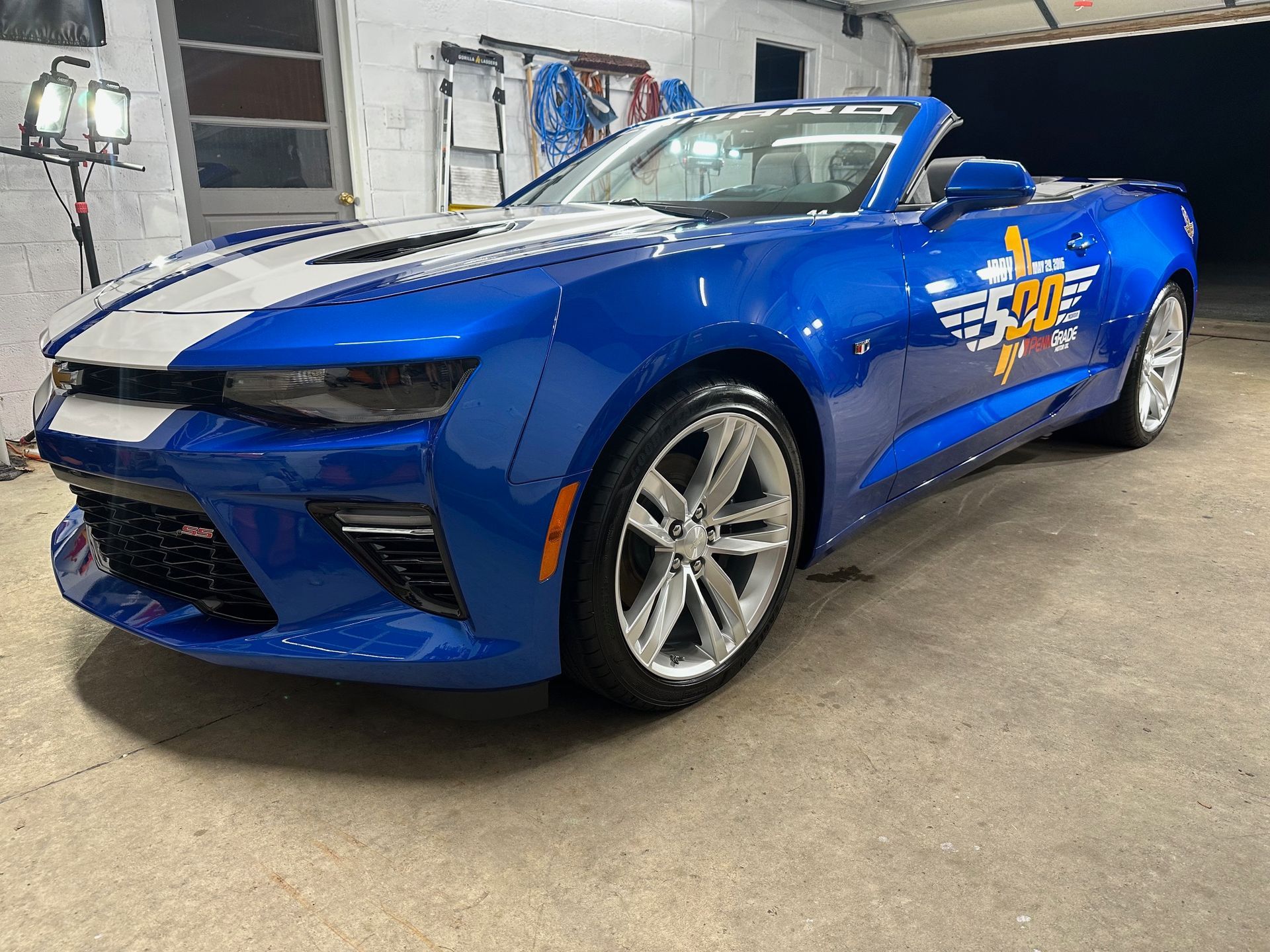 Blue convertible car with white racing stripe, parked indoors.