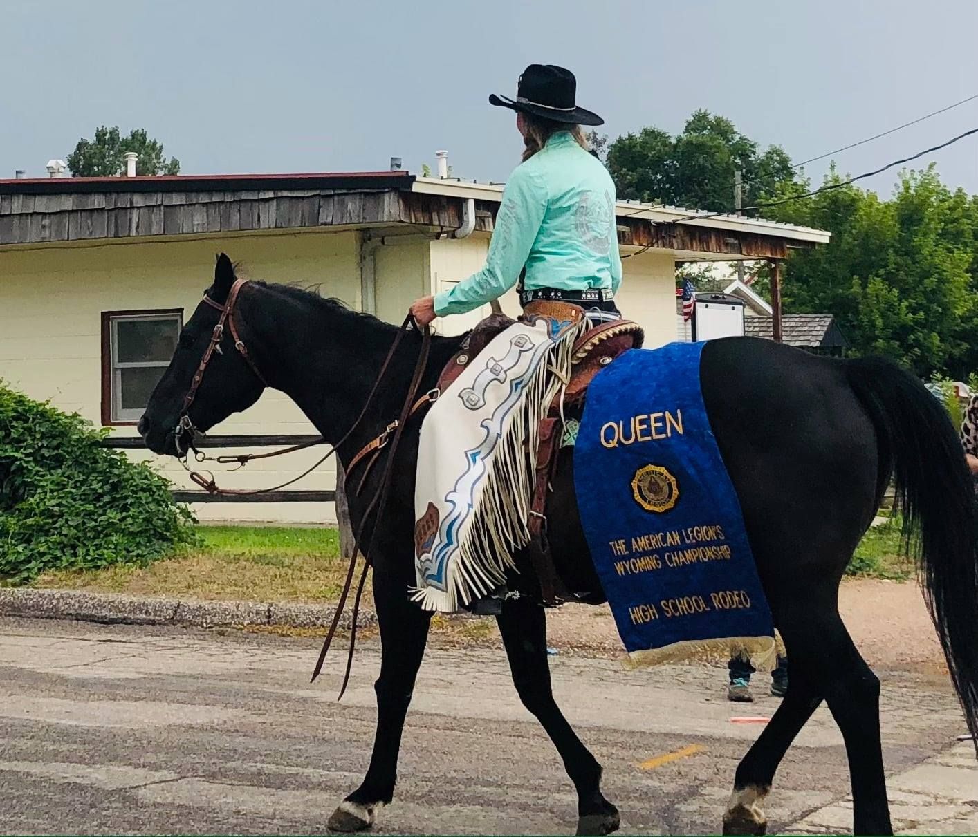 A man is riding a black horse with a blue sash that says queen