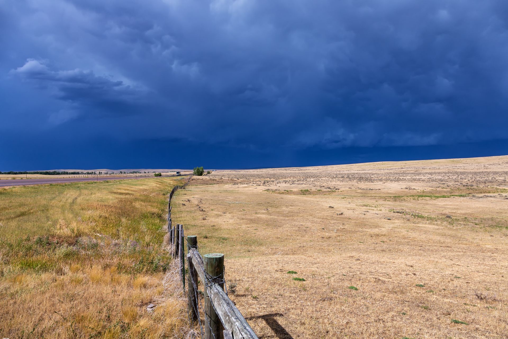 A wooden fence surrounds a dry grassy field with a cloudy sky in the background.