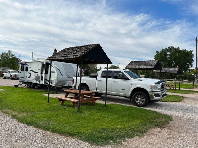 A white truck is parked next to a trailer and a picnic table.