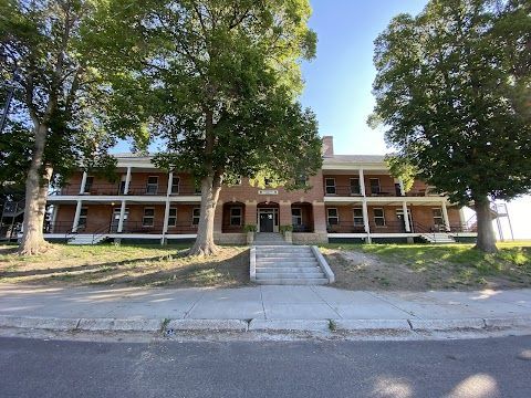 A large brick building with stairs leading up to it is surrounded by trees.