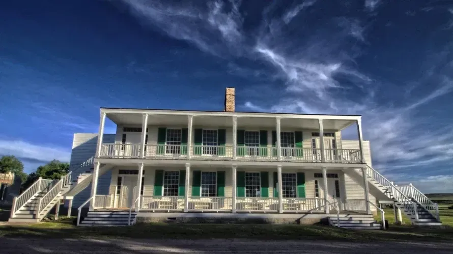 A large white house with green shutters and stairs