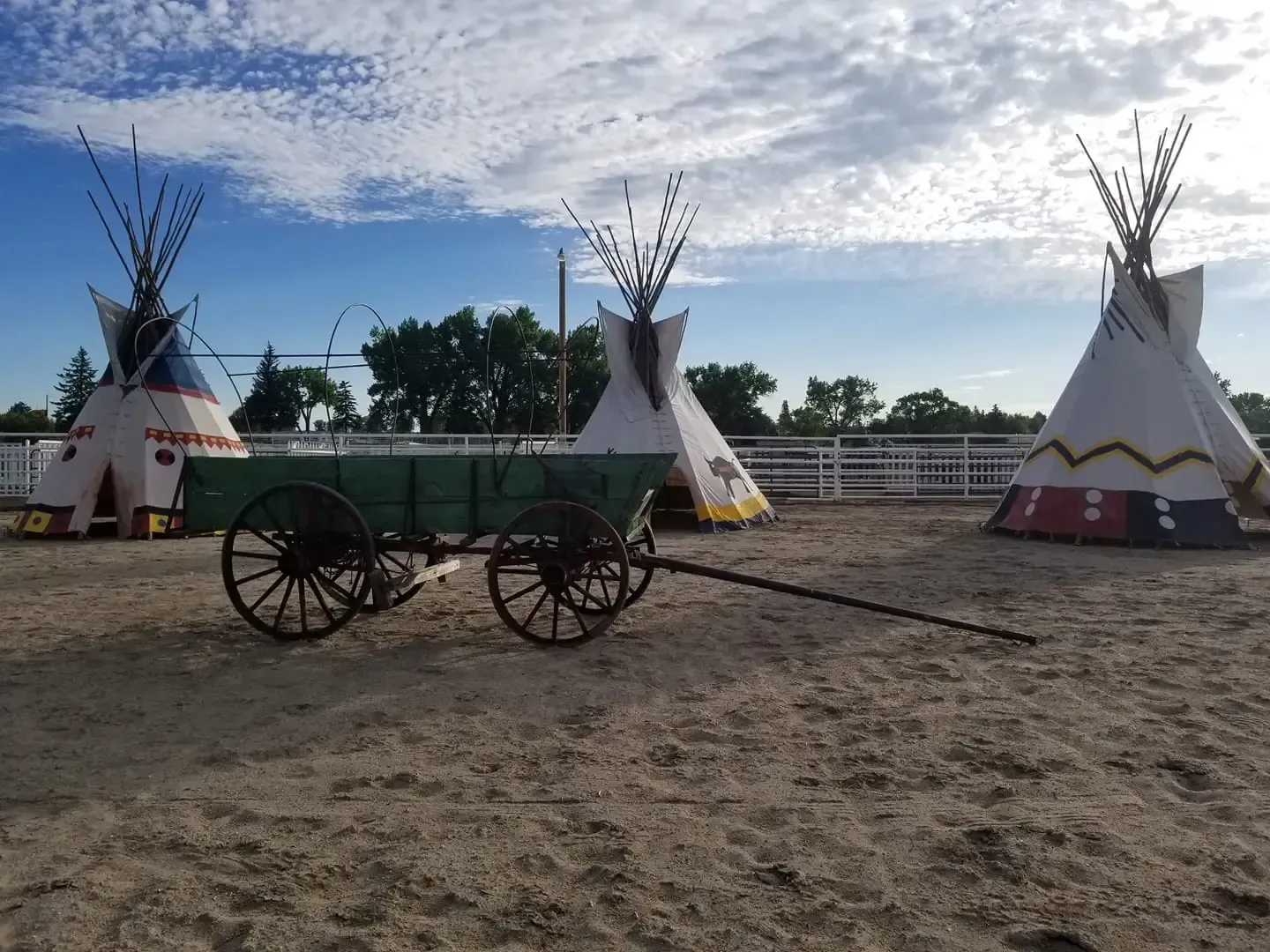 A wagon and tepees in a dirt field.