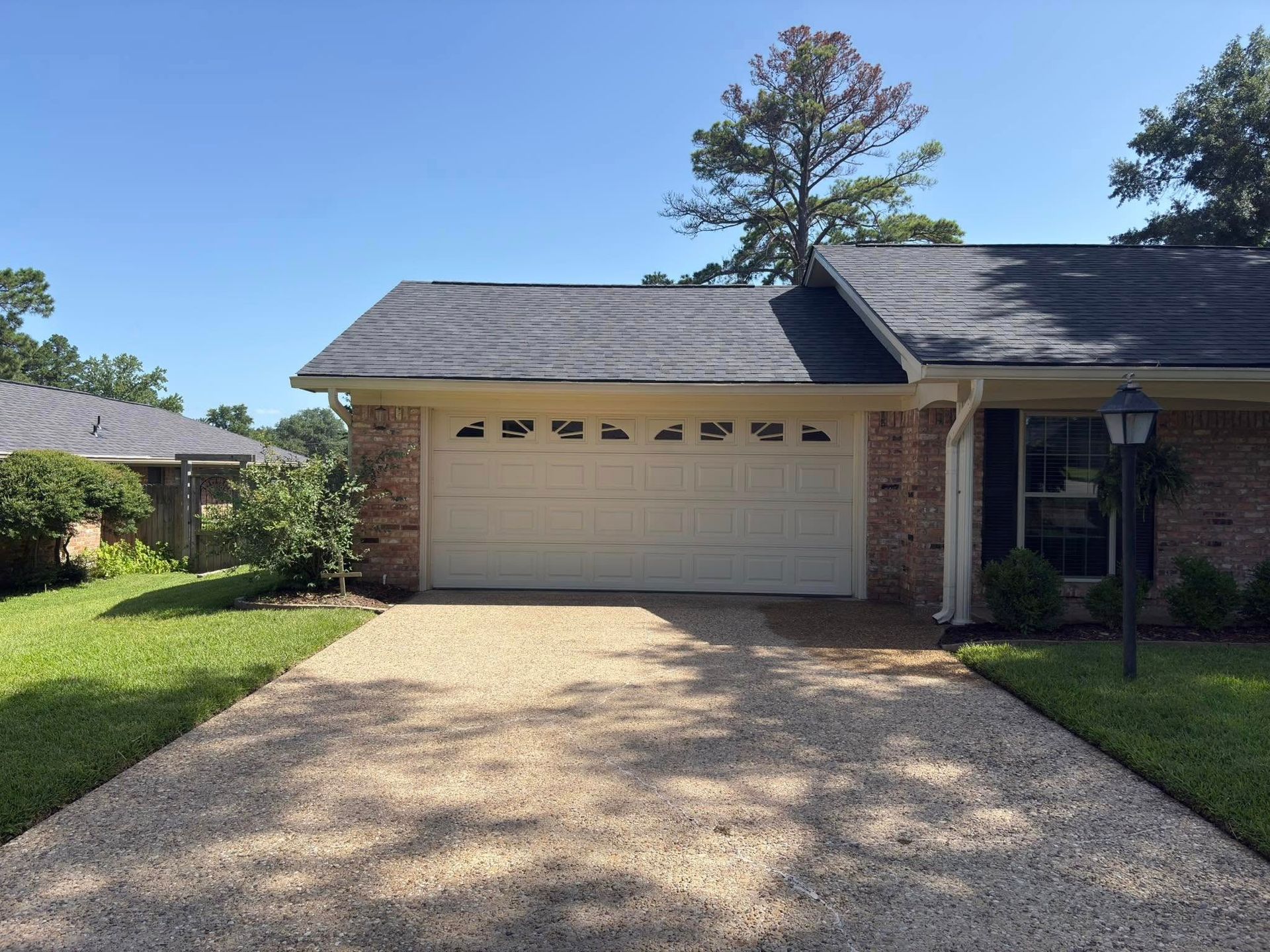 Suburban house with a two-car garage, gravel driveway, and green lawn on a sunny day