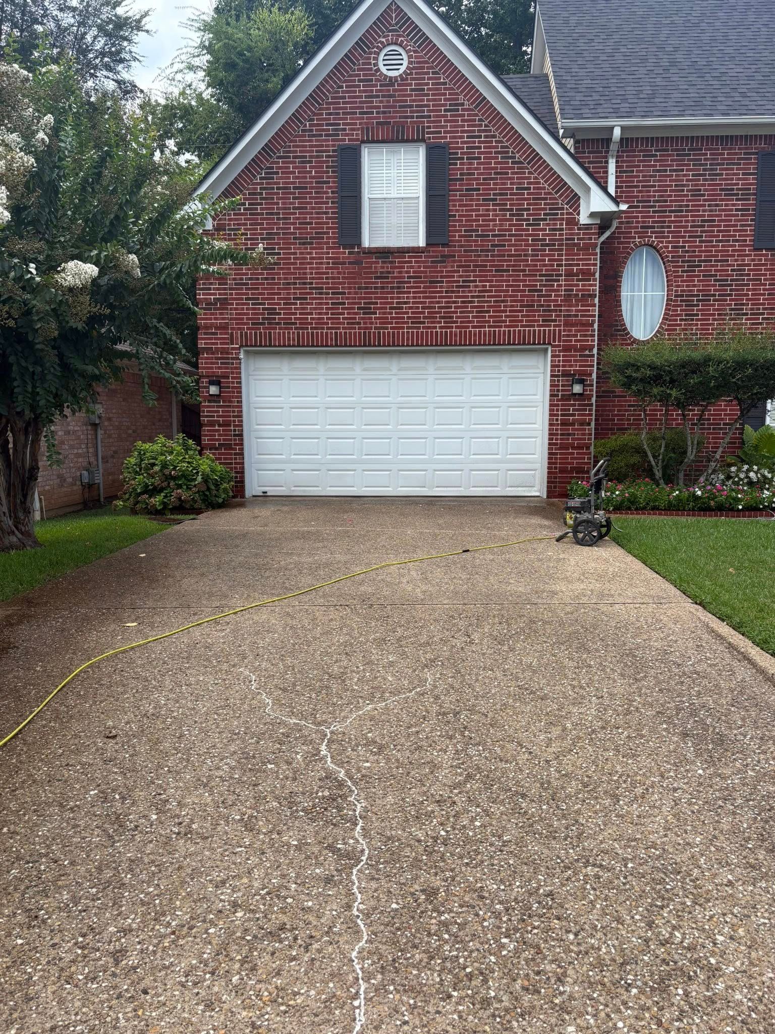 Brick house with white garage door and stone driveway, framed by trees and a small front lawn