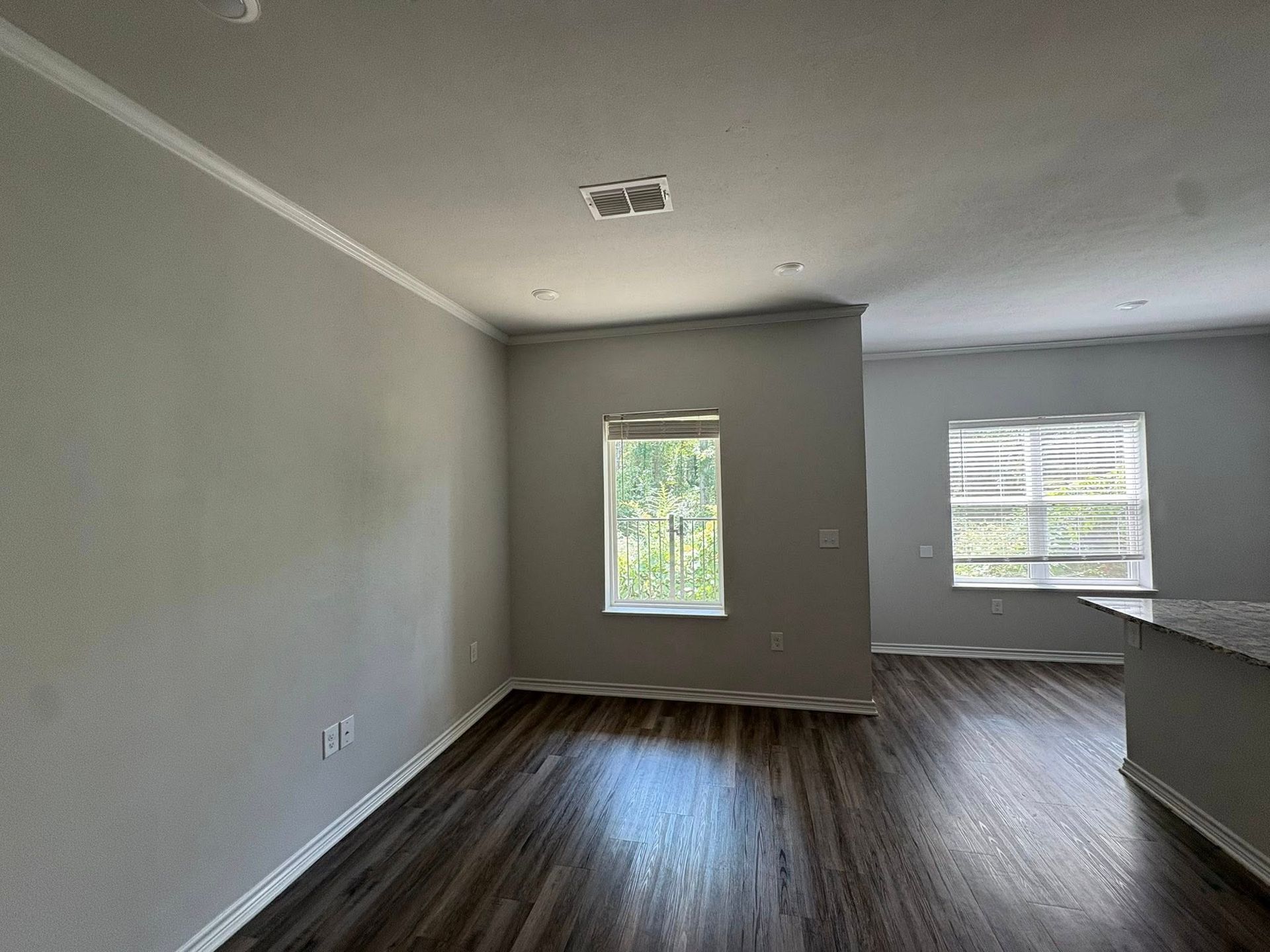Empty unfurnished room with gray walls, wood floor, and two windows letting in daylight