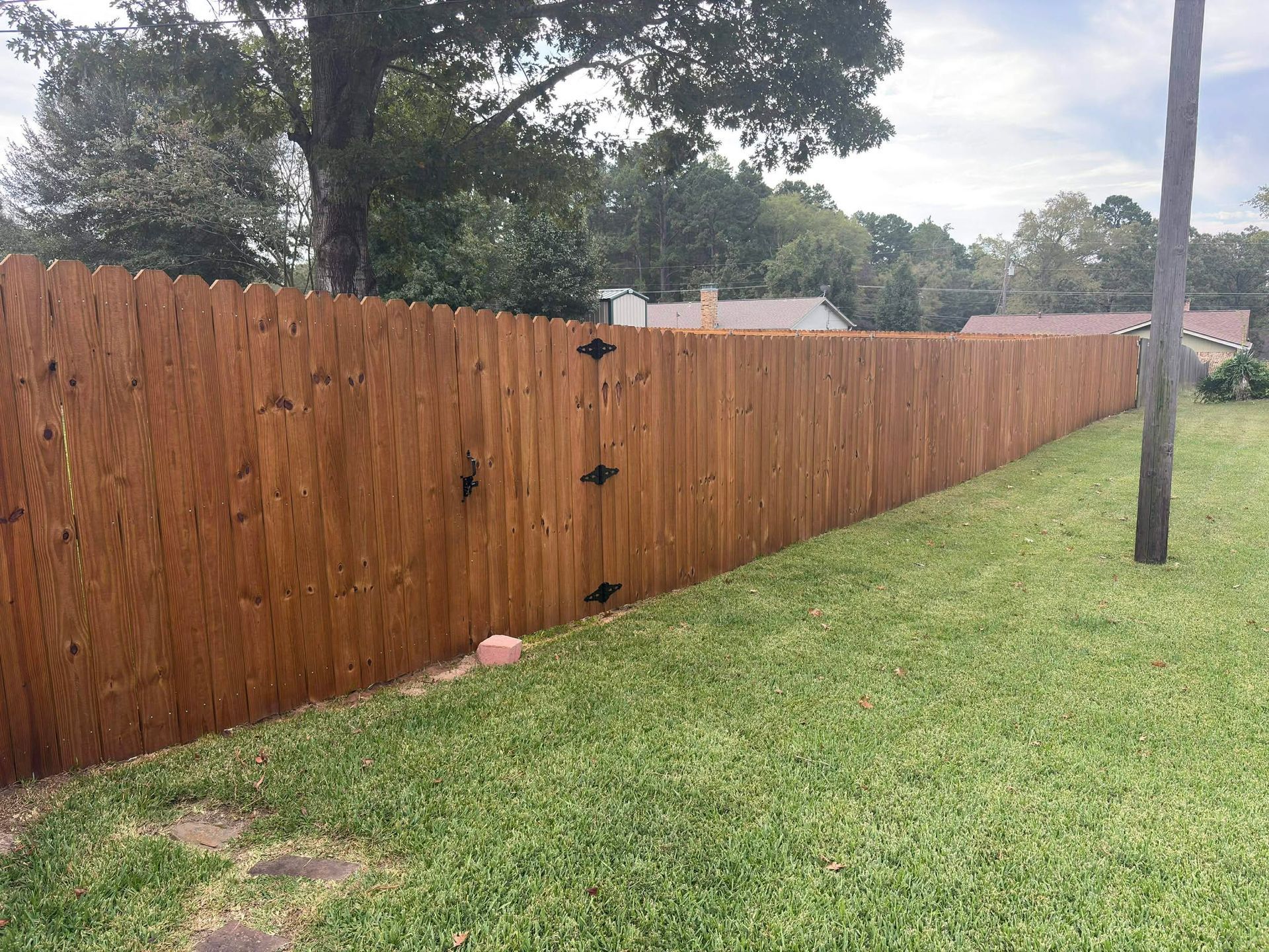 Wooden privacy fence along a grassy yard with trees and a utility pole in the background.