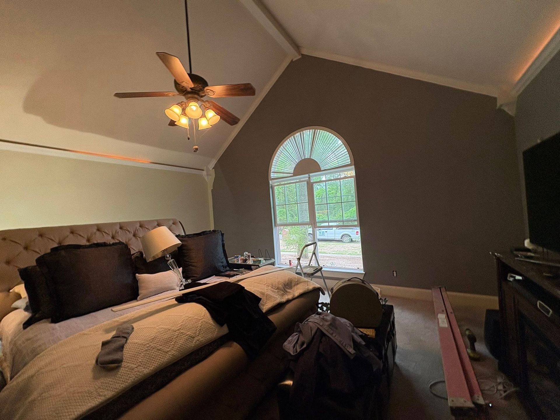 Bright bedroom with vaulted ceiling, arched window, king bed, and ceiling fan light