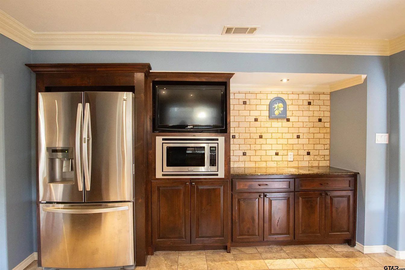 Kitchen with stainless steel refrigerator, built-in microwave and dark wood cabinets on blue walls.