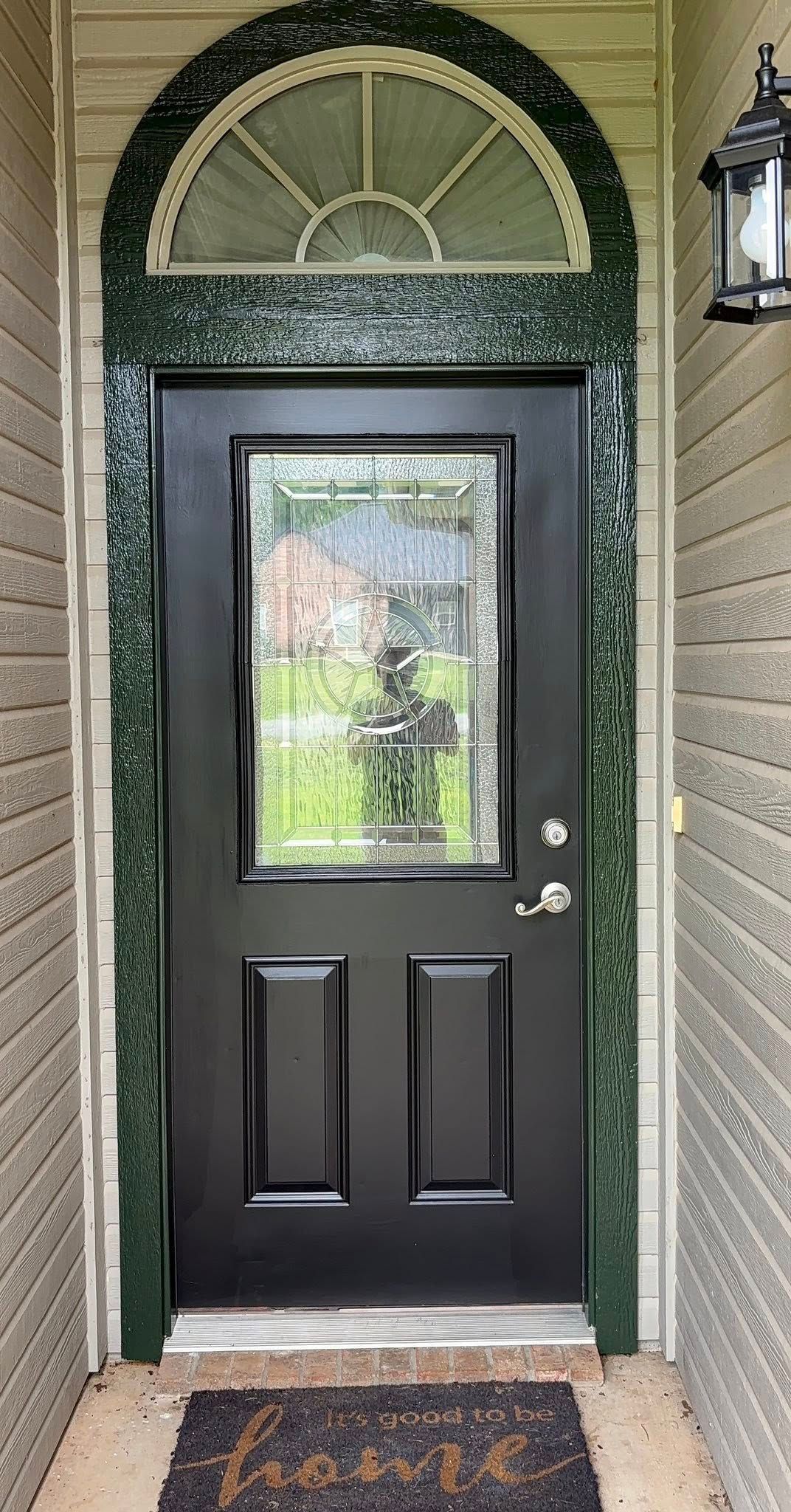 Black front door with glass panel and arched transom in a narrow brick entryway