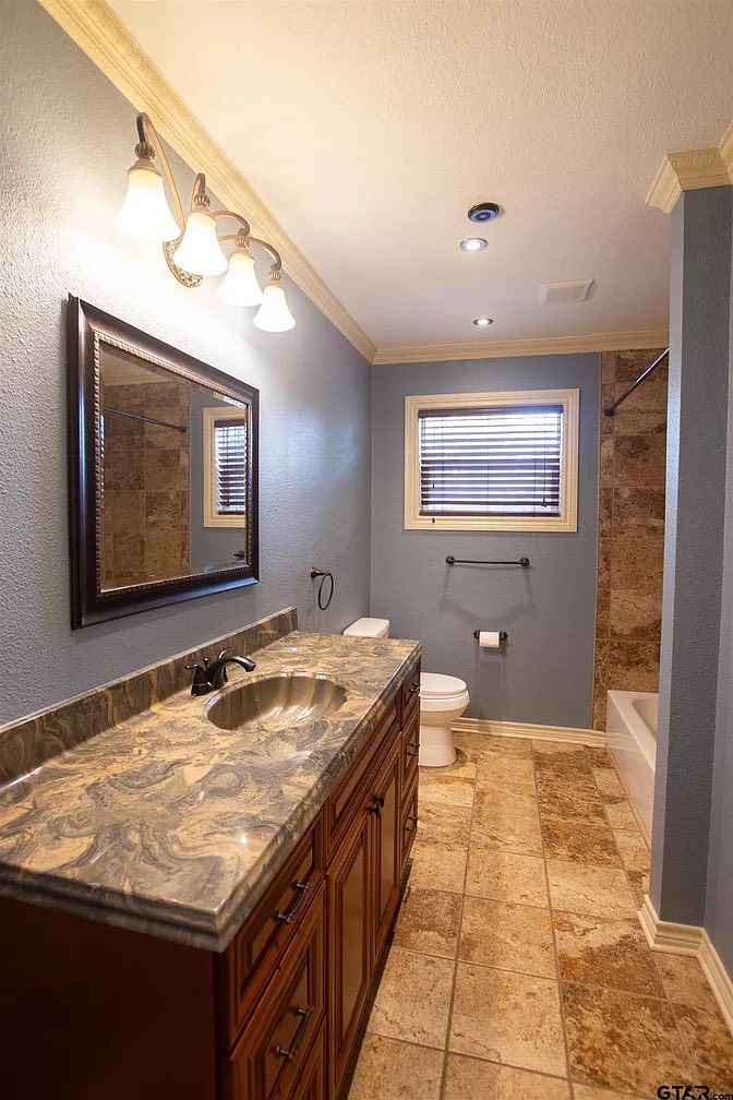 Bathroom with marble vanity, wall mirror, tiled floor, and window with blinds