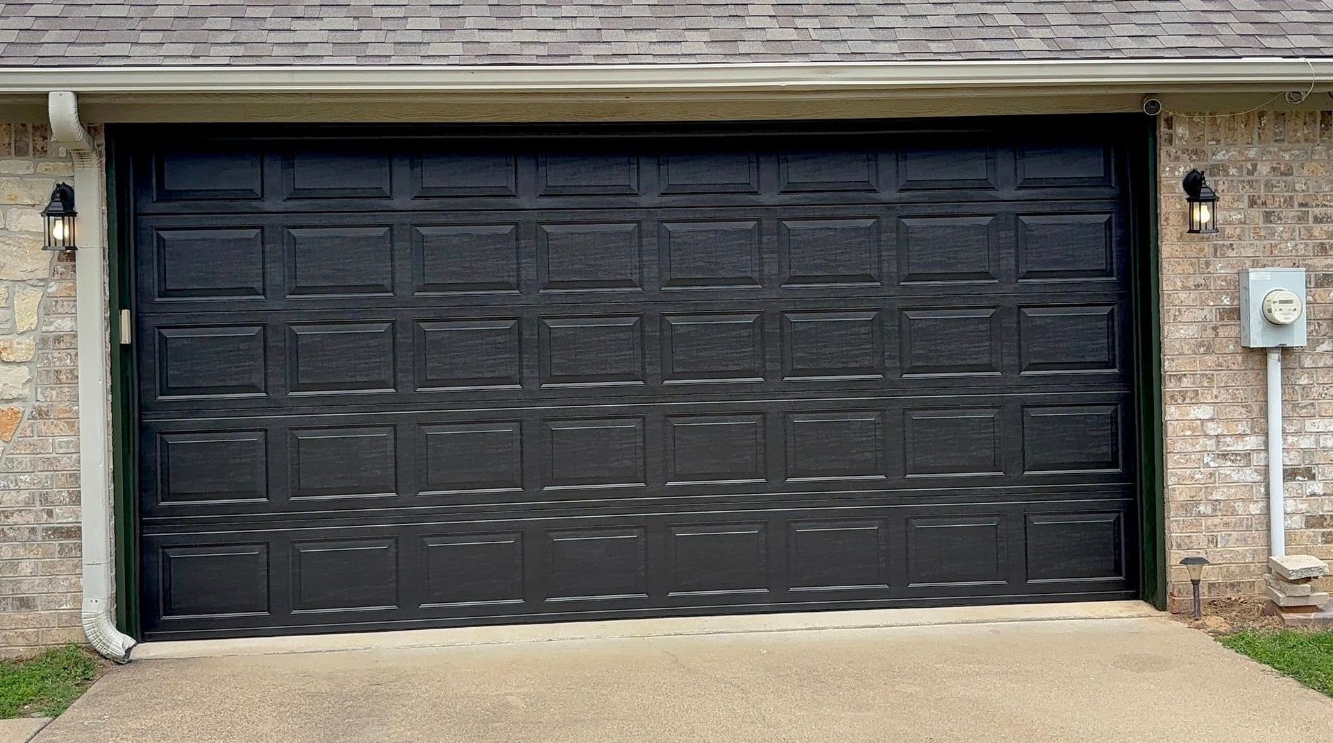 Black double garage door set in a stone house facade with driveway in front