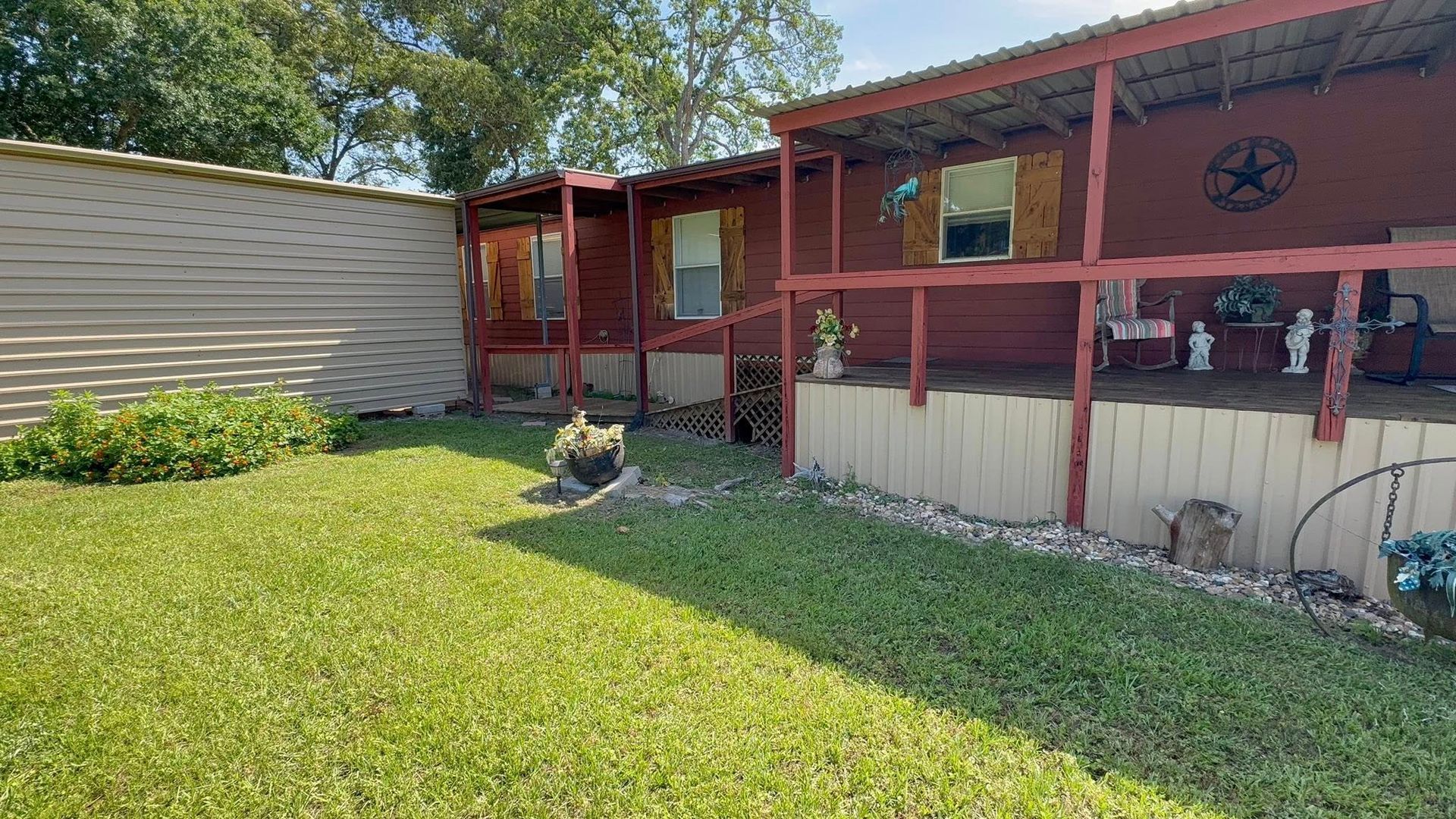 Red house with porch and fenced yard beside a beige mobile home, under sunny blue sky