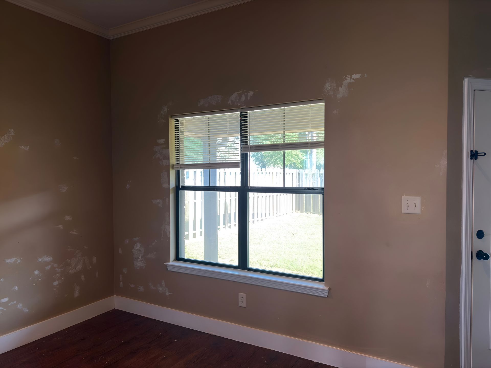 Empty room with brown walls, white trim, a window, and patchy paint spots