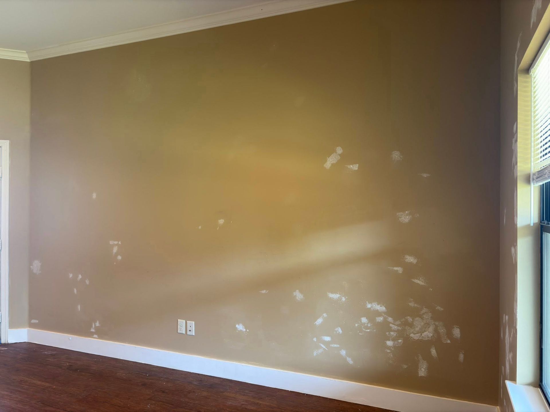 Empty beige room with white baseboards and patchy paint on the wall