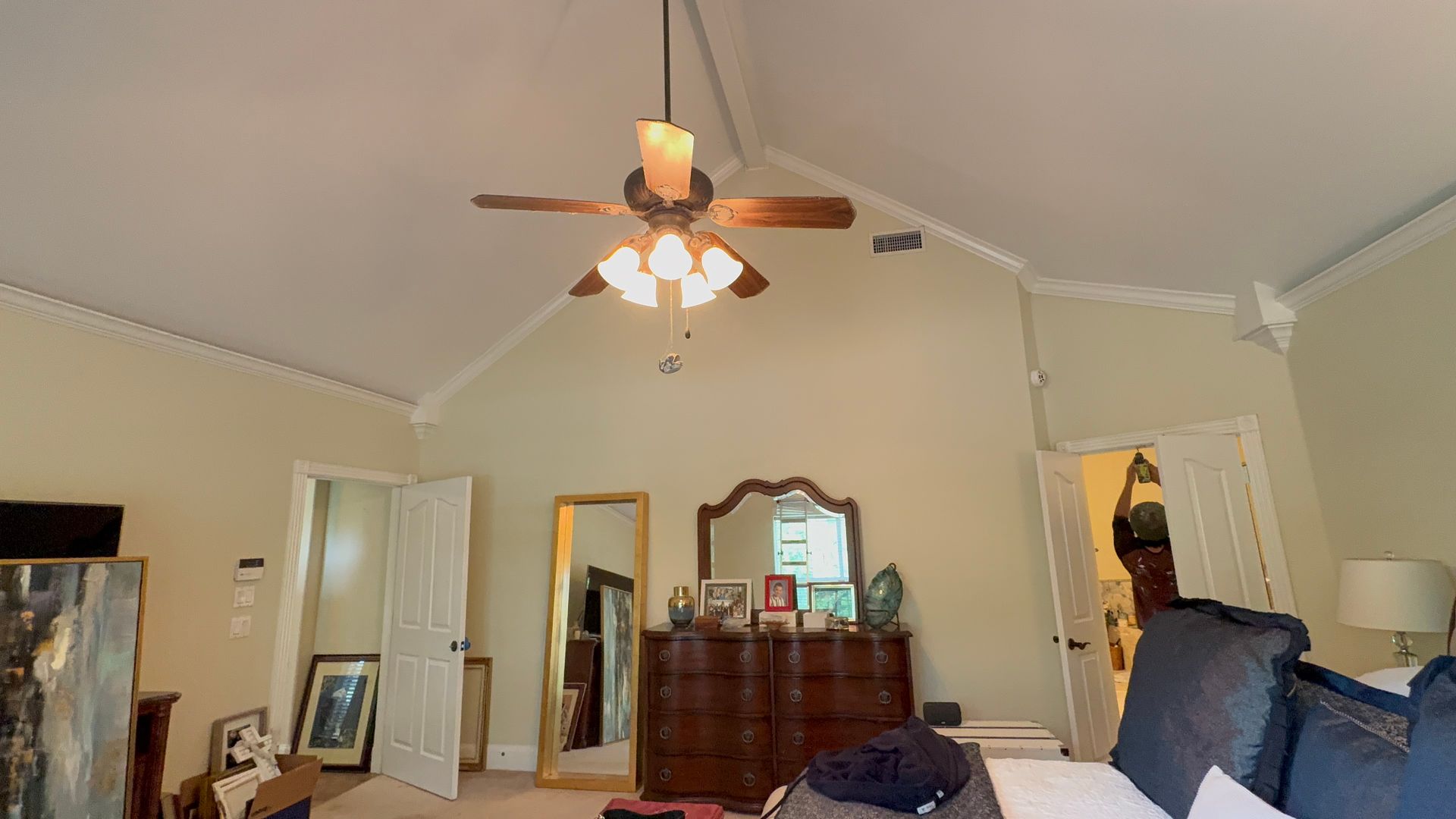 Bedroom with white walls, ceiling fan, dresser, mirror, open closet, and chair in a cluttered room.