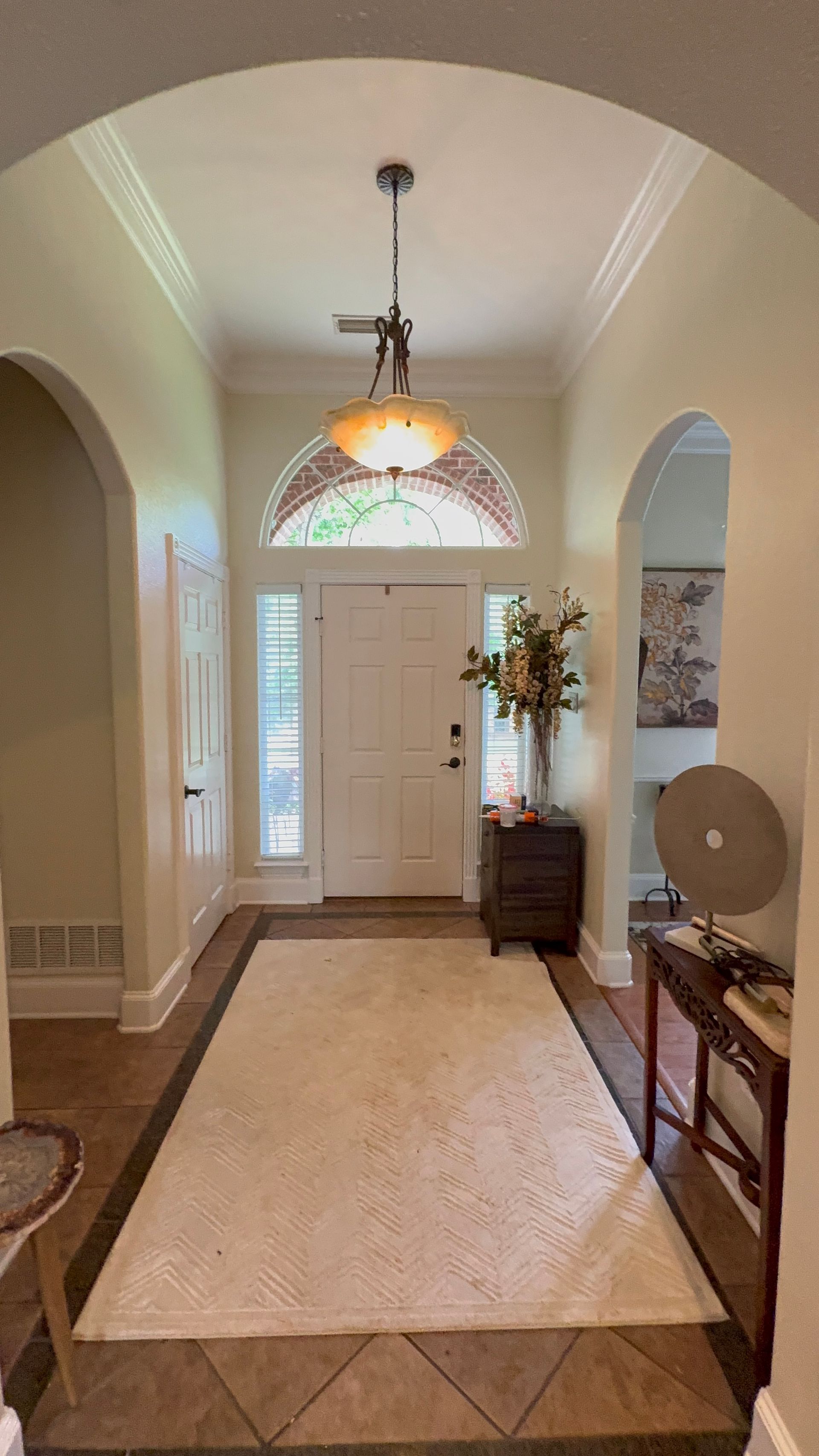 Bright entry hallway with arched doorway, front door, hanging light, rug, and small table