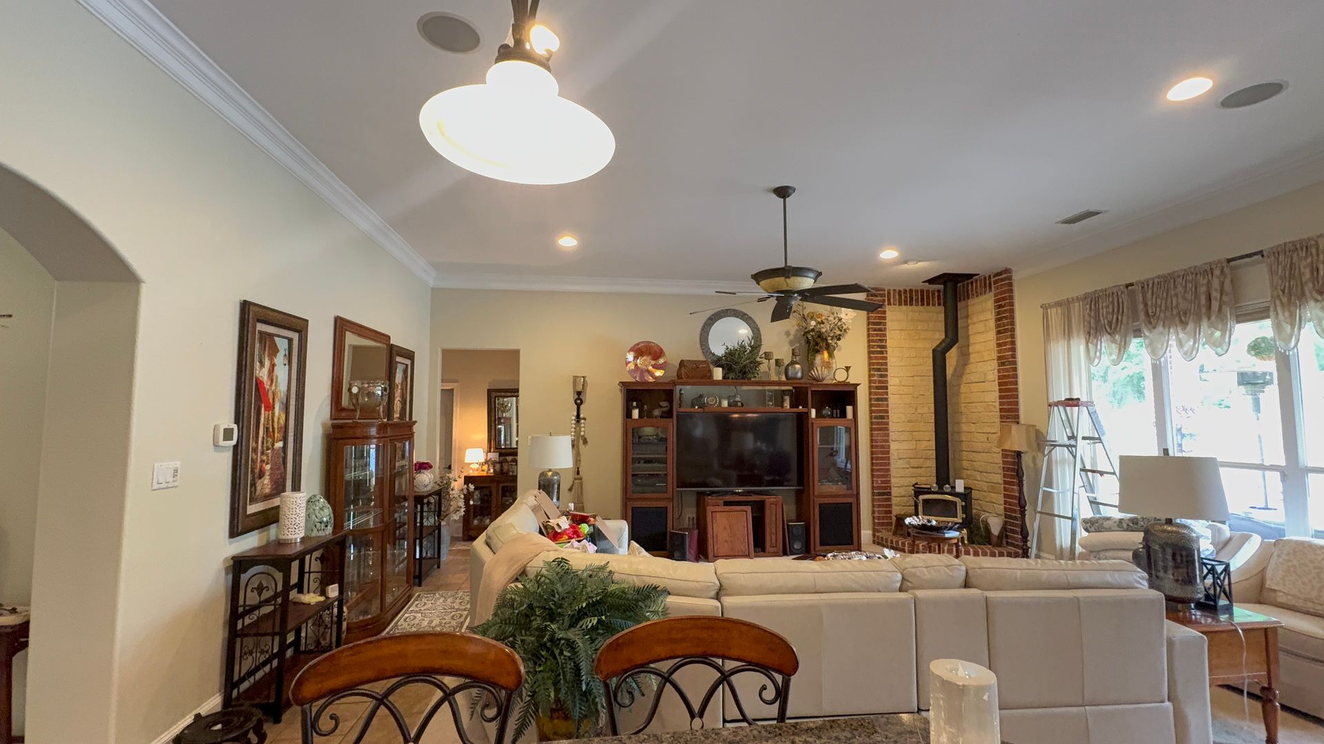 Bright living room with white sofa, chandelier, display cabinet, and large window with curtains