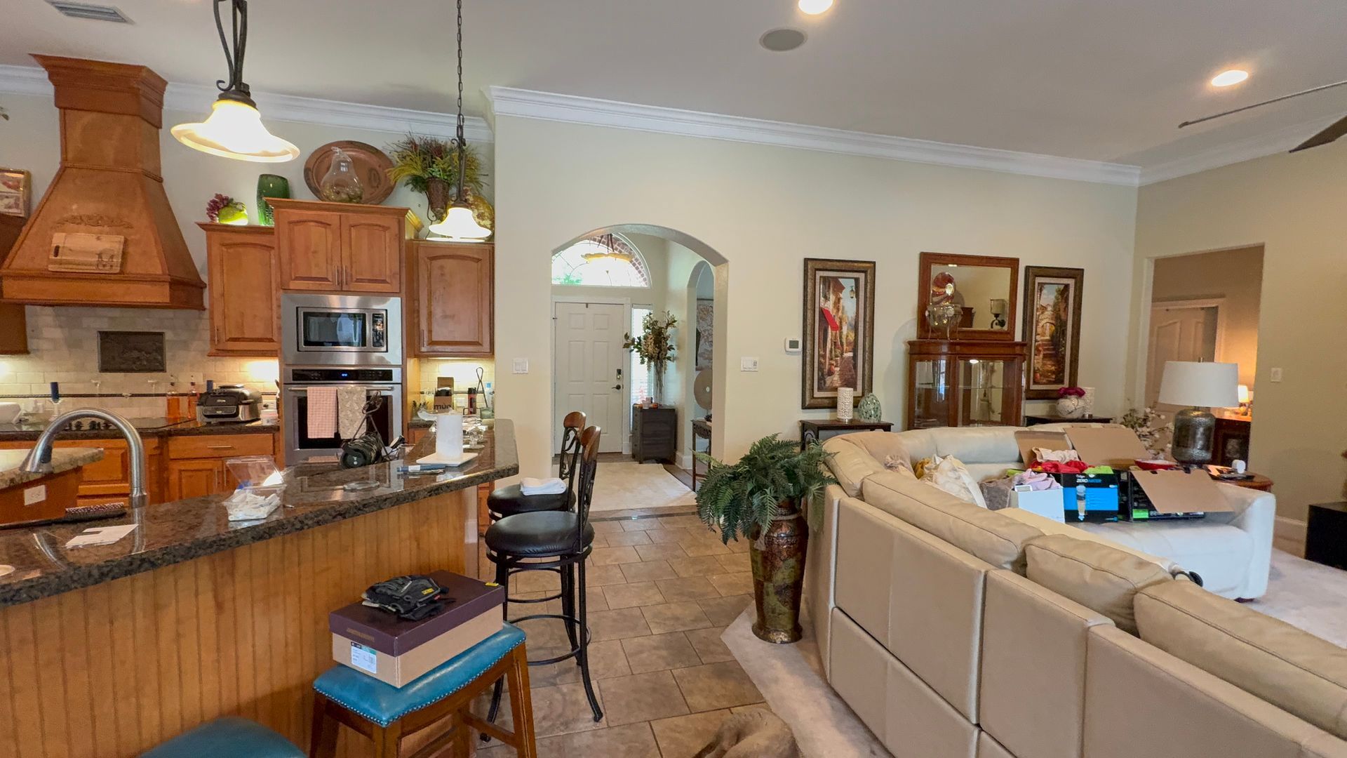 Open kitchen and living room with beige sectional, wooden cabinets, and arched doorway